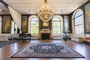 A grand ballroom with arched windows, a crystal chandelier, a classic fireplace, elegant wall murals, and a polished wood floor