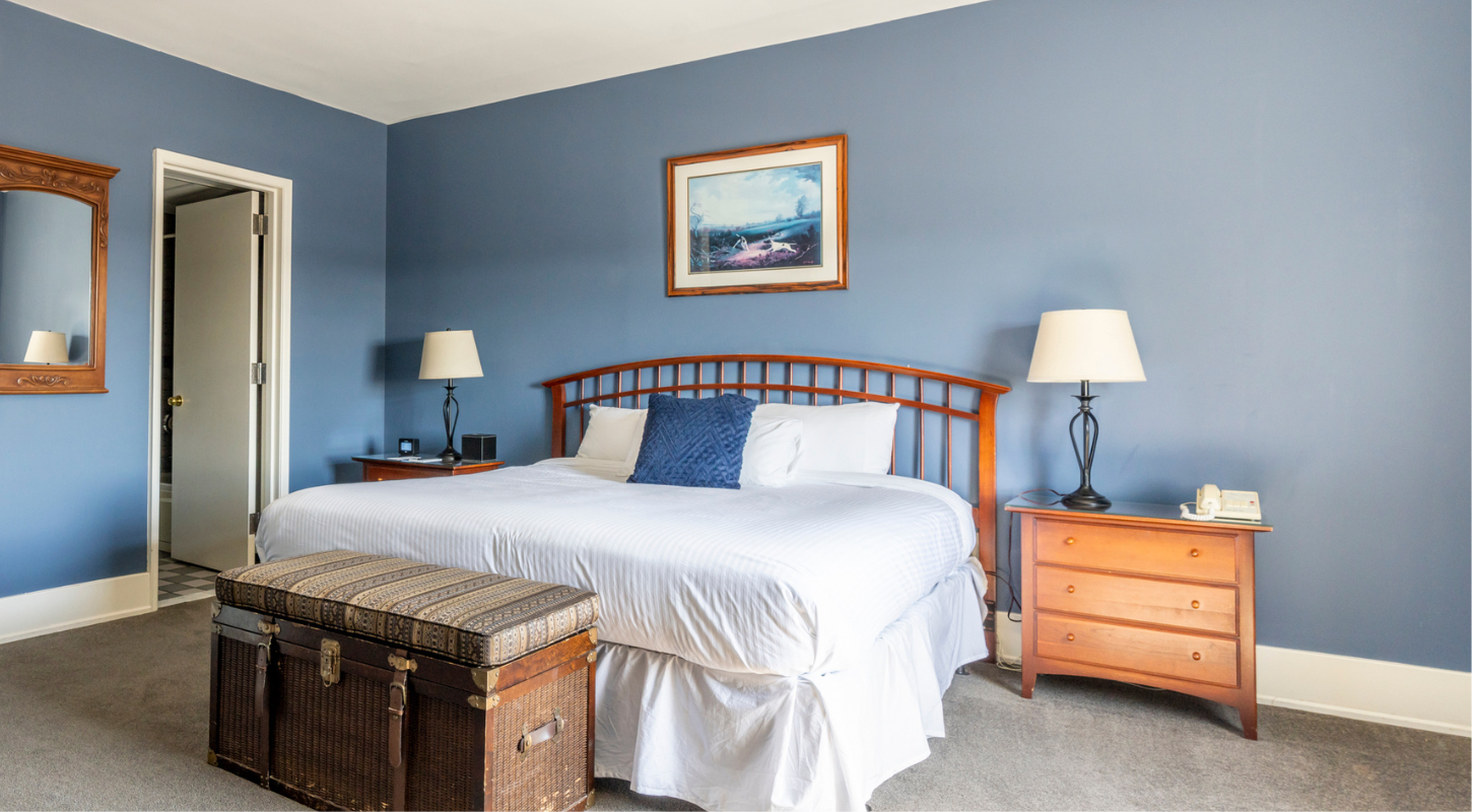 Luxuriously appointed guest room at the Inn on Broadway featuring blue walls and coordinating throw pillows on a plush white bedspread