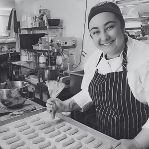 Smiling pastry chef Rachael wearing a striped apron and piping frosting onto a baking sheet of cookies